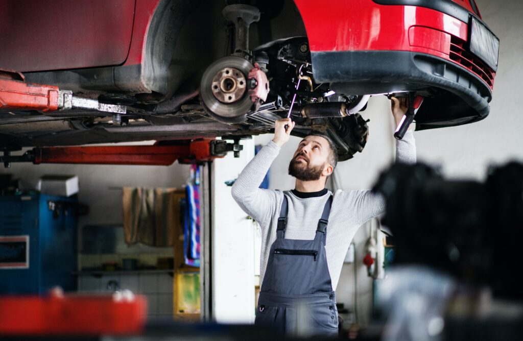 Mechanic repairing exhaust system under car at Southall Autos and Tyres, specializing in exhaust pipe leaks, catalytic converter issues, muffler damage, and more.